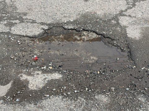 Deep Pothole Filled with Muddy Water on a Damaged Asphalt Road. Concept of Poor Urban Infrastructure, Street Maintenance Issues, Road Safety Hazards, and Neglected Transportation Systems in the City