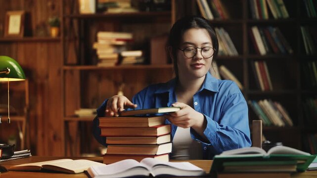 Asian woman bringing stack of books for studying in a library, diligent student