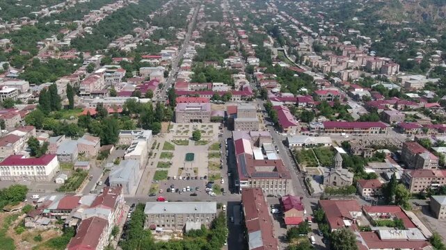 Beautiful aerial drone view of Goris, a picturesque city nestled in a green valley surrounded by majestic mountains in Armenia, featuring a long main street and red roofs.