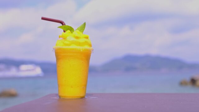 Smoothie made from fresh mango fruits against the backdrop of a seascape. Fruit and yoghurt ice cream decorated with leaves. Glass of tropical dessert close-up.