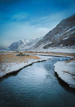 Scenic winter view of a winding river flowing through snow-covered plains towards majestic mountains in Hunder, Nubra Valley, Ladakh, India under a blue sky 