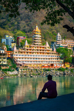 Silhouette of a man sitting by the holy Ganges River, admiring the majestic 13-story Trimbakeshwar Temple (Tera Manzil) in Rishikesh, Uttarakhand, India.