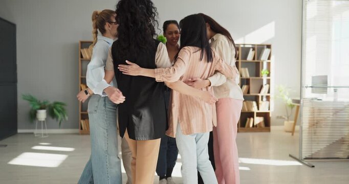 Women team hug showing support, unity, collaboration. In a bright office, a group of colleagues forms a circle to celebrate progress and motivate teamwork in a meeting. Clear unity concept.