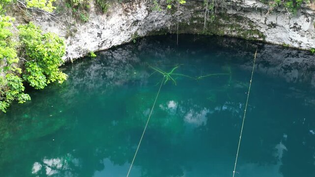 Aerial view focusing on deep blue cenote water and surrounding rocky borders. Perfect for tourism promotion and natural beauty visuals.