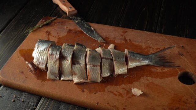 Fresh fish fillet being sliced on a wooden cutting board with a sharp knife and herbs in the background, showcasing the preparation process
