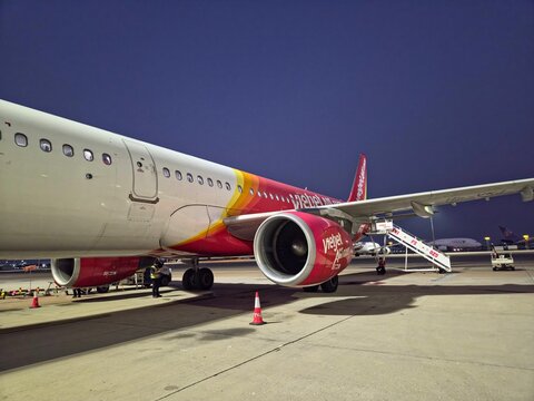 Low-angle view of a VietJet Air Airbus A321 parked on an airport tarmac at night with boarding stairs attached on March 26, 2026 in Sichuan Province, China.