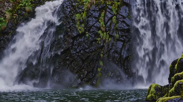 Close up mossy cliff waterfall with dark basalt rocks, emerald moss and soft mist spilling into calm alpine pool secluded forest setting, gentle ambient motion, soothing soundscape ideal