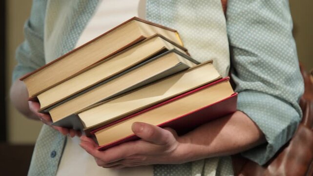 Female student holding stack of textbooks in hands close-up