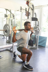 Fototapeta premium African American man performing barbell lunge at gym, wearing grey shirt dark shorts