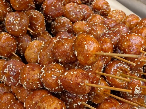 Tang You Guo Zi, a famous Chengdu street food, features deep-fried glutinous rice balls on skewers, coated in a shiny red sugar glaze and white sesame seeds. 