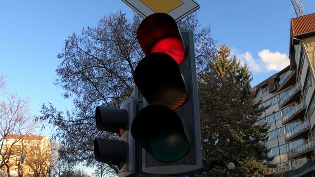 A traffic light at an intersection, the red light is on, then the yellow light comes on, then both go out and the green light comes on