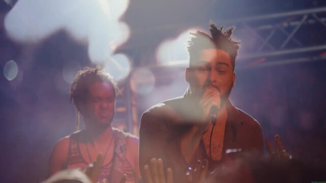 Music starting driving lead vocalist singing into mic, gesturing, engaging audience amid bokeh haze