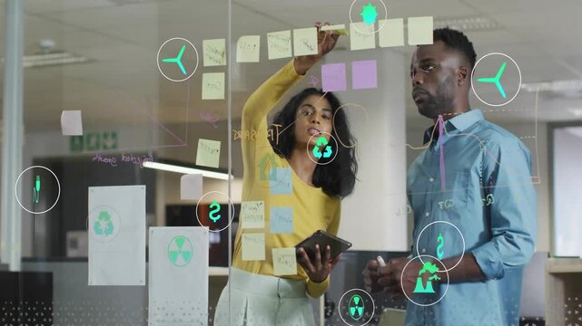 Woman placing purple note using tablet, man pointing as teal icons animating on glass for business