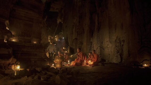 Buddhist monks holding candles and praying during a religious ceremony inside a cave in Cambodia