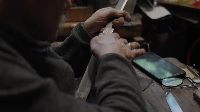 Elderly craftsman working in his old workshop, carefully restoring collectible Japanese bladed weapons