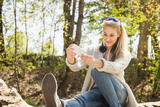 Young Woman Sitting on a Tree Stump Taking a Selfie in Nature.