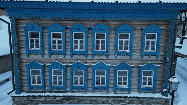 Drone view of a charming wooden house with blue window frames covered in snow on a winter day