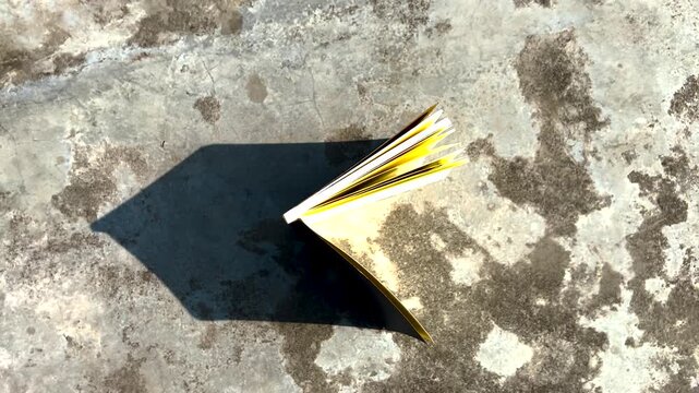 Small book with pages fluttering in the wind casting a sharp shadow on a rustic stone surface in high angle shot