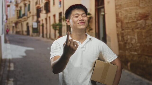 Man holding a cardboard box shows middle finger on a narrow cobblestone street, smirking while carrying a package; defiance attitude.