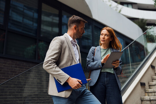 Business colleagues having an active discussion while standing on the stairs in front of a modern office building.