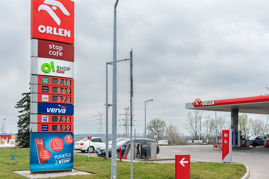 ZABRZE, POLAND - MARCH 29, 2026: A large red Orlen gas station pylon displaying current fuel prices in the foreground. Cars parked near the refueling pumps on a cloudy spring day.