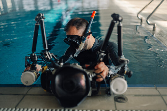Male underwater photographer with snorkeling mask and professional camera housing with strobe light filming in pool