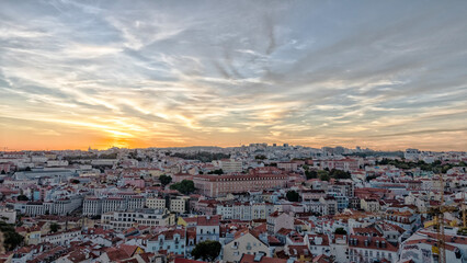 Fototapeta premium Aerial-style elevated view overlooking the historic city of Lisbon, Portugal, with colorful buildings, terracotta rooftops, and the Tagus River stretching across the horizon at sunset