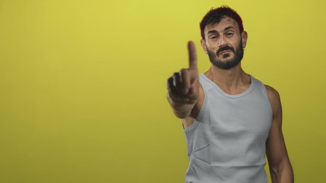 Man points index finger at camera in yellow studio wearing grey tanktop and beard, frontal pose; stern warning.