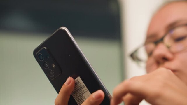 Student studying silently. Young learner analyzing study references on mobile device in quiet space. Student with glasses carefully examining and highlighting notes on phone in serene setting