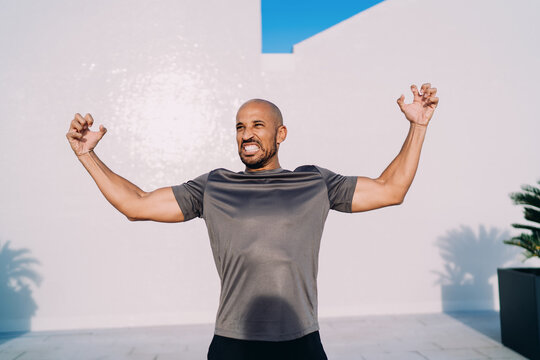Portrait of smiling man in sportswear looking away, athlete resting on modern balcony, positive mindset and mental health, urban wellness, confident male model in morning sunlight.