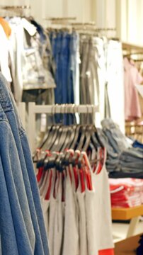 Department store denim jackets on display rack, shopper browsing and assistant restocking under bright fluorescent lights, stacked tees and jeans in background, dynamic retail energy and promotional