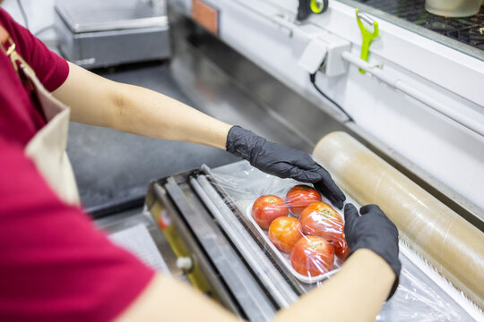 Shop assistant packing fresh tomatoes in plastic wrap