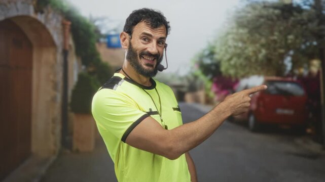 Referee man pointing finger with whistle on lanyard in street with headset mic and smile; playful guidance.