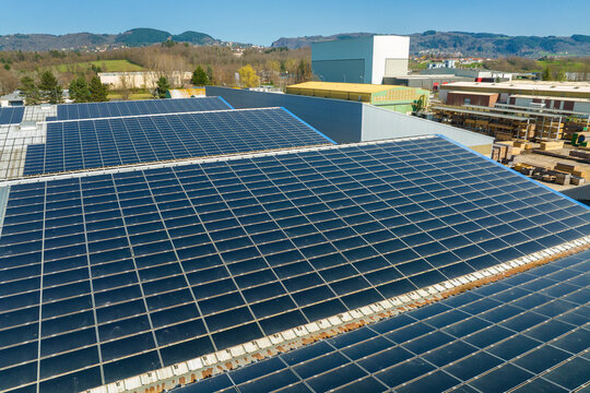 Aerial view of solar power plant with blue photovoltaic panels mounted on industrial building roof for producing green ecological electricity. Production of sustainable energy concept