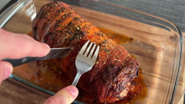 Close-up of slicing juicy pork roulade with knife and fork in a glass dish. Concept of homemade cooking, ready meal serving, food texture, and traditional cuisine.