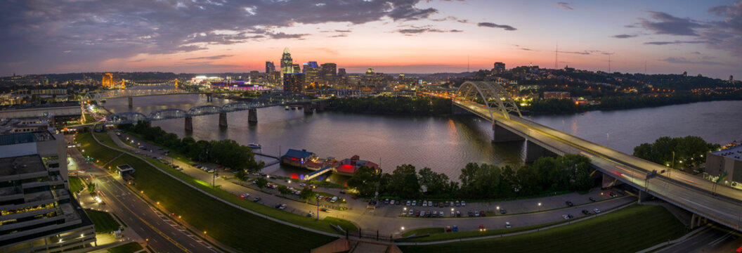 Night urban landscape of downtown district of Cincinnati city in Ohio, USA. Skyline with bridge traffic and brightly illuminated high skyscraper buildings in modern American megapolis