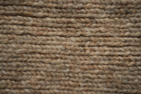 brown texture of knitted wool fabric as a background, white smooth symmetrical lines of hand-knitted needlework pattern	
