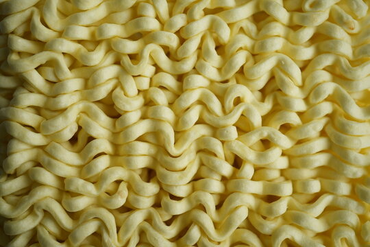 macro texture of instant noodles with repeating wavy pattern. Close-up of dry ramen showing detailed structure and soft beige tones. Organic abstract background perfect for food concepts, packaging de