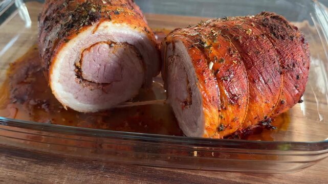 Close-up of sliced hot pork roulade in glass baking dish with steam and juices. Juicy meat texture, homemade food concept, cooking process, fresh roast, comfort meal.