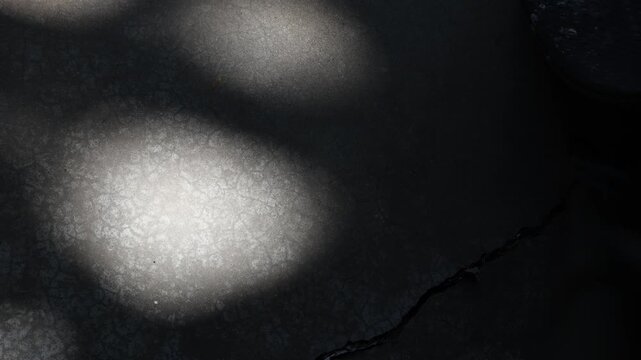 4k video clip 25 second b roll of circular sunlight shinning and flickering on dark cement pavement. 