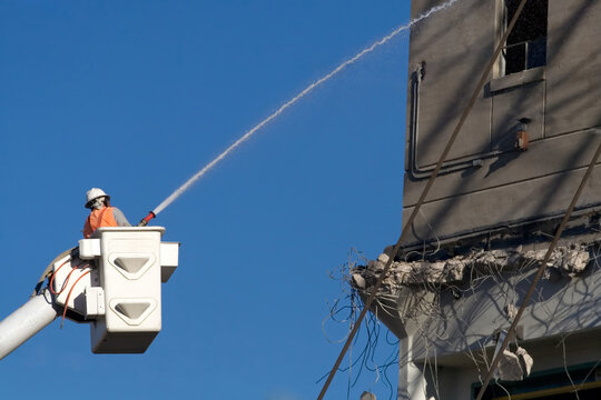 Construction Worker Spraying Water During Building Demolition Dust Control