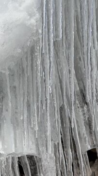 Close-up of vertical rows of clear ice icicles. Frozen water droplets and melting white snow on top. Textured ice surface with reflections. Cold winter atmosphere