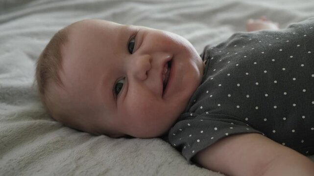 Young child lying comfortably in nursery setting. Joyful infant with rosy cheeks and gentle giggle in soft natural light. Smiling baby in an adorable dotted outfit, cozy gray environment