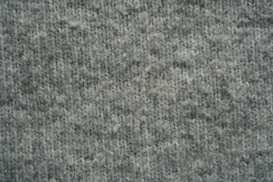 macro texture of grey acrylic knitted fabric with visible pilling. Close-up of synthetic textile surface showing soft fibers and small fabric pills. Detailed and realistic texture with neutral tones, 