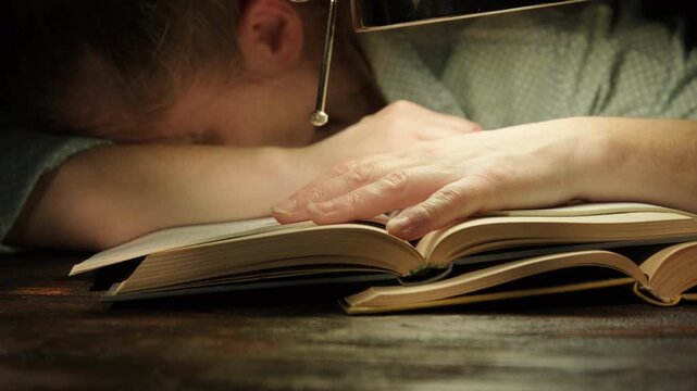 Tired female student sleeping on textbooks sitting at desk late at night while studying doing homework