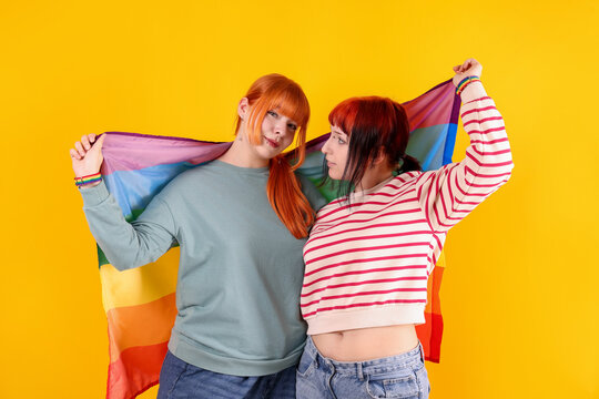 Lovely lesbian couple with rainbow flag on yellow background. LGBT concept