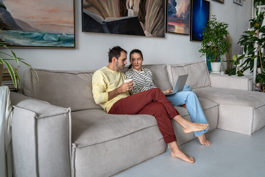 Relaxed man and woman married couple planning renovation at home, choosing new furniture and textiles online on laptop, browsing doing research and discussing prices. make decision together as family.
