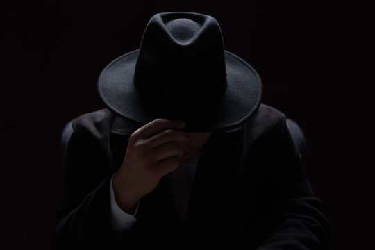 Man wearing stylish hat in armchair on black background