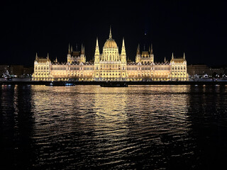 Fototapeta premium Night view of the Hungarian Parliament building in Budapest with reflections on the Danube River and illuminated historic architecture.