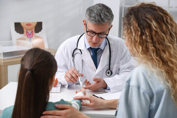 Fototapeta premium Endocrinologist in glasses checking little girl's blood sugar level with lancet pen while her mother supporting her at white desk in clinic